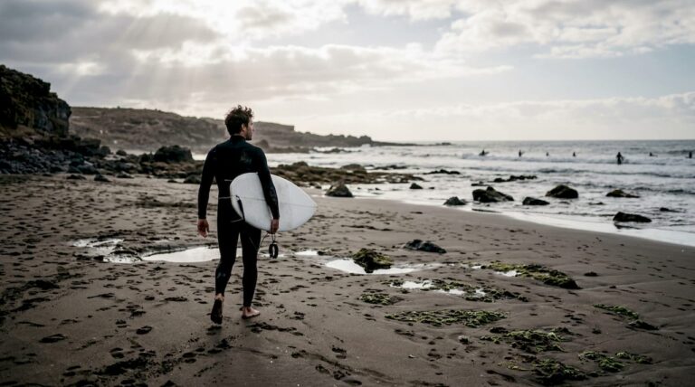 Un surfista recorre la orilla de una playa de arena negra en Tenerife.